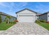 Exterior view of a home featuring a two-car garage, brick paver driveway, and well-maintained landscaping at 9566 Coastline Way, Parrish, FL 34219