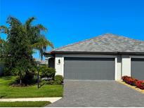 Exterior view of a well-kept home featuring a grey two car garage, pavers, manicured lawn, and vibrant landscaping at 16087 Sunny Day Dr, Bradenton, FL 34211