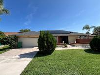 Charming single-story home featuring solar panels, a two-car garage, and a well-manicured lawn under a clear blue sky at 19358 Edgewater Dr, Port Charlotte, FL 33948