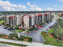 Stunning exterior view of a condominium complex with a red roof, lush landscaping and ample parking at 21405 Olean Blvd # 224, Port Charlotte, FL 33952