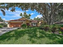 Charming single-story home featuring a terracotta tile roof, beautiful landscaping, and a large shade tree at 1674 Cottonwood Trl, Sarasota, FL 34232