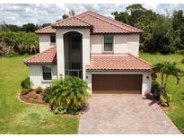 Two-story home with a red tile roof, paver driveway, and manicured lawn in a lush, green landscape at 20940 Valore Ct, Venice, FL 34293