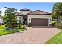 Charming single-story home with a red tile roof, brown garage door, brick driveway, and lush landscaping at 4735 Cassio Ct, Bradenton, FL 34211