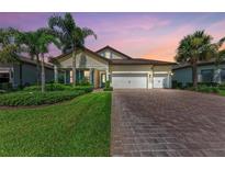 Beautiful single-story home featuring a three-car garage, lush landscaping, and a brick paver driveway at 7781 Grande Shores Dr, Sarasota, FL 34240