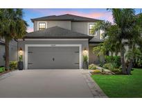 Two-story gray home featuring a gray garage door, tropical landscaping, and a paver driveway at 16419 Paynes Mill Dr, Bradenton, FL 34211