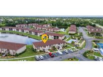 Scenic aerial view of a condo community with lush landscaping, lake, swimming pool, and tennis courts at 25100 Sandhill Blvd # V202, Punta Gorda, FL 33983