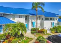 Bright white exterior with blue metal roof, lush tropical landscaping, and covered parking at 840 Audubon Dr, Bradenton, FL 34209