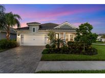 Charming single-Gathering home featuring a two-car garage, paver driveway, lush landscaping, and twilight sky at 2586 Wild Cherry Path, Sarasota, FL 34240
