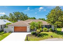 Charming single-story home featuring a wood-paneled garage door, manicured lawn, and lush landscaping at 891 Faulkwood Ct, Sarasota, FL 34232