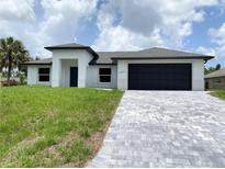 Beautiful single-story home featuring a paver driveway, black garage door, minimalist landscaping, and a stucco facade at 2692 Pretzel Ln, North Port, FL 34286