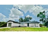 Well-manicured lawn and a charming one-story house featuring an attached garage and a dark roof against a cloudy blue sky at 5009 Jody Ave, North Port, FL 34288