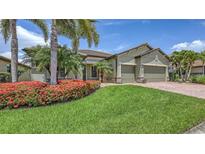 Beautiful home with lush landscaping, featuring vibrant red flowers and palm trees in the front yard at 11200 Whimbrel Ln, Sarasota, FL 34238