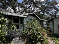 Shows the exterior of the dilapidated one story home surrounded by trees and overgrown foliage at 2026 Seminole S Blvd, St Petersburg, FL 33705