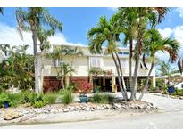 Charming yellow two-story home with lush landscaping, palm trees, and a welcoming entrance at 701 Marbury Lane, Longboat Key, FL 34228