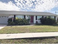 White house with red door, two-car garage, and landscaping at 21277 Edgewater Dr, Port Charlotte, FL 33952