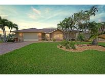 Single-story home with a large grassy yard, paver driveway, and tropical landscaping at 446 Valletta Ct, Punta Gorda, FL 33950