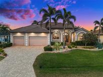Charming home featuring a three-car garage, lush landscaping, and a well-manicured lawn with palm trees at 1422 Kittiwake Dr, Punta Gorda, FL 33950