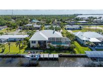 Back of waterfront home featuring a screened-in pool, boat dock, and well-maintained lawn with palm trees at 4431 Gardner Dr, Port Charlotte, FL 33952