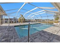 A screened-in pool features a tile border and paver surround with waterfront view and clear blue sky at 4107 Rock Creek Dr, Port Charlotte, FL 33948