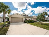 Inviting beige single story home featuring a wide driveway, lush landscaping, and two-car garage at 7393 West Lenox Cir, Punta Gorda, FL 33950