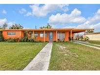 Charming one-story home featuring a bright orange exterior, blue door and lush green lawn at 520 Sharon Cir, Port Charlotte, FL 33952