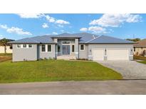 Beautiful gray home featuring a three-car garage, well-manicured lawn, and blue-gray trim at 7363 N Moss Rose, Punta Gorda, FL 33955