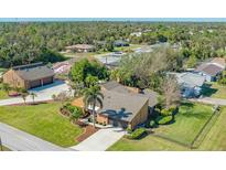An aerial view of a tan home surrounded by lush green grass, palm trees, and other homes in a serene neighborhood at 1525 Hinton St, Port Charlotte, FL 33952