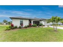Landscaped front yard featuring a well-maintained lawn, colorful flowers, and a stately palm tree, complementing the home's architecture at 16265 Juarez Cir, Punta Gorda, FL 33955