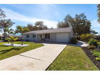 Charming single-story home featuring a well-manicured lawn and concrete driveway, with mature trees in the background at 18379 Meyer Ave, Port Charlotte, FL 33948