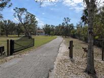 Long driveway leading to a charming home, framed by mature trees and a secure gate at 24485 Tangerine Ave, Punta Gorda, FL 33980