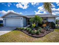 Charming single-story home with attached garage and manicured tropical landscaping in front yard at 129 Barre Nw Dr, Port Charlotte, FL 33952