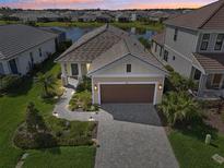 Beautiful home featuring a paver driveway, manicured landscaping, and a serene lake view backdrop at 10112 Canaveral Cir, Sarasota, FL 34241