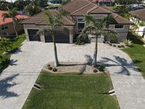 Gorgeous home featuring a paver driveway, two-car garage, lush lawn, and lovely landscaping with mature palm trees at 556 Monaco Dr, Punta Gorda, FL 33950