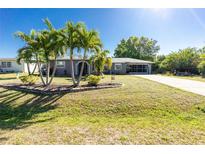 Charming single-story home featuring a well-manicured lawn, mature palm trees, and neutral toned facade under a bright blue sky at 2550 Ivanhoe St, Port Charlotte, FL 33952