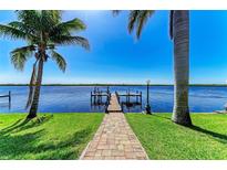 Waterfront property featuring a private dock extending into the serene water, framed by swaying palm trees and a well-manicured lawn at 3790 Peace River Dr, Punta Gorda, FL 33983