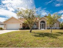 Inviting single-story home with a two-car garage, manicured lawn, and mature trees under a blue sky at 16571 Cape Horn Blvd, Punta Gorda, FL 33955