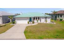 Charming single-story home with a green metal roof, manicured lawn, and paved driveway at 18662 Arapahoe Cir, Port Charlotte, FL 33948