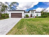 Beautifully landscaped front yard and modern home exterior with a two-car garage and paver driveway at 1384 Alpinia Rd, North Port, FL 34288