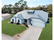 Beautiful single-story home featuring a well-manicured lawn, metal roof, arched entryway, and attached two-car garage at 908 Tropical Nw Cir, Port Charlotte, FL 33948