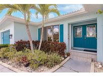 Charming home featuring a vibrant blue front door, lush landscaping, and a welcoming entrance, complemented by tropical palm trees at 103 Colony Point Dr, Punta Gorda, FL 33950