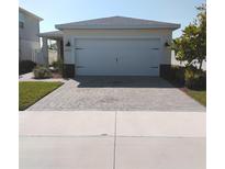 Home exterior featuring a two car garage, brick paver driveway, manicured lawn, and neutral paint at 43735 Cattleman Dr, Punta Gorda, FL 33982