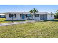 Charming single-story home with a lush green lawn, quaint blue door, and attached garage at 225 Garden Nw Ave, Port Charlotte, FL 33952