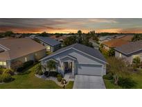 Inviting single-story home with a two-car garage, complemented by a well-maintained lawn and tropical landscaping at sunset at 24055 Buckingham Way, Punta Gorda, FL 33980