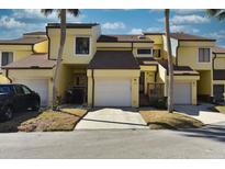 Inviting yellow townhouse with a private garage, a brick-paved driveway, and mature palm trees in a well-maintained community at 25188 Marion Ave # 1013, Punta Gorda, FL 33950