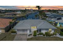 Waterfront home featuring a gray tile roof, screened garage, a concrete driveway, and mature landscaping at sunset at 2350 W Marion Ave, Punta Gorda, FL 33950