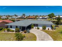 Waterfront home featuring mature landscaping, tile roof, and circular driveway surrounded by lush tropical foliage at 1206 Winward Ct, Punta Gorda, FL 33950