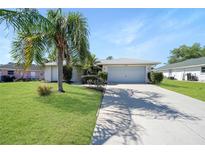 Well-maintained single-story home featuring a lush lawn, mature palm tree, and a two-car garage with a long driveway at 3753 Aba Ln, North Port, FL 34287