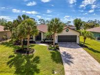 Charming single-story home featuring a well-manicured lawn, mature palm trees, and a patterned driveway leading to a two-car garage at 32 Long Meadow Ln, Rotonda West, FL 33947