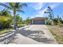 Charming single-story home featuring a two-car garage, long driveway, and lush landscaping with palm trees at 1357 Le Pera Rd, Englewood, FL 34223