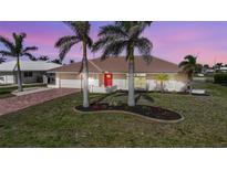 Inviting home featuring a bright red door, lush lawn, mature palm trees, and paver driveway leading to a two car garage at 530 Matares Dr, Punta Gorda, FL 33950